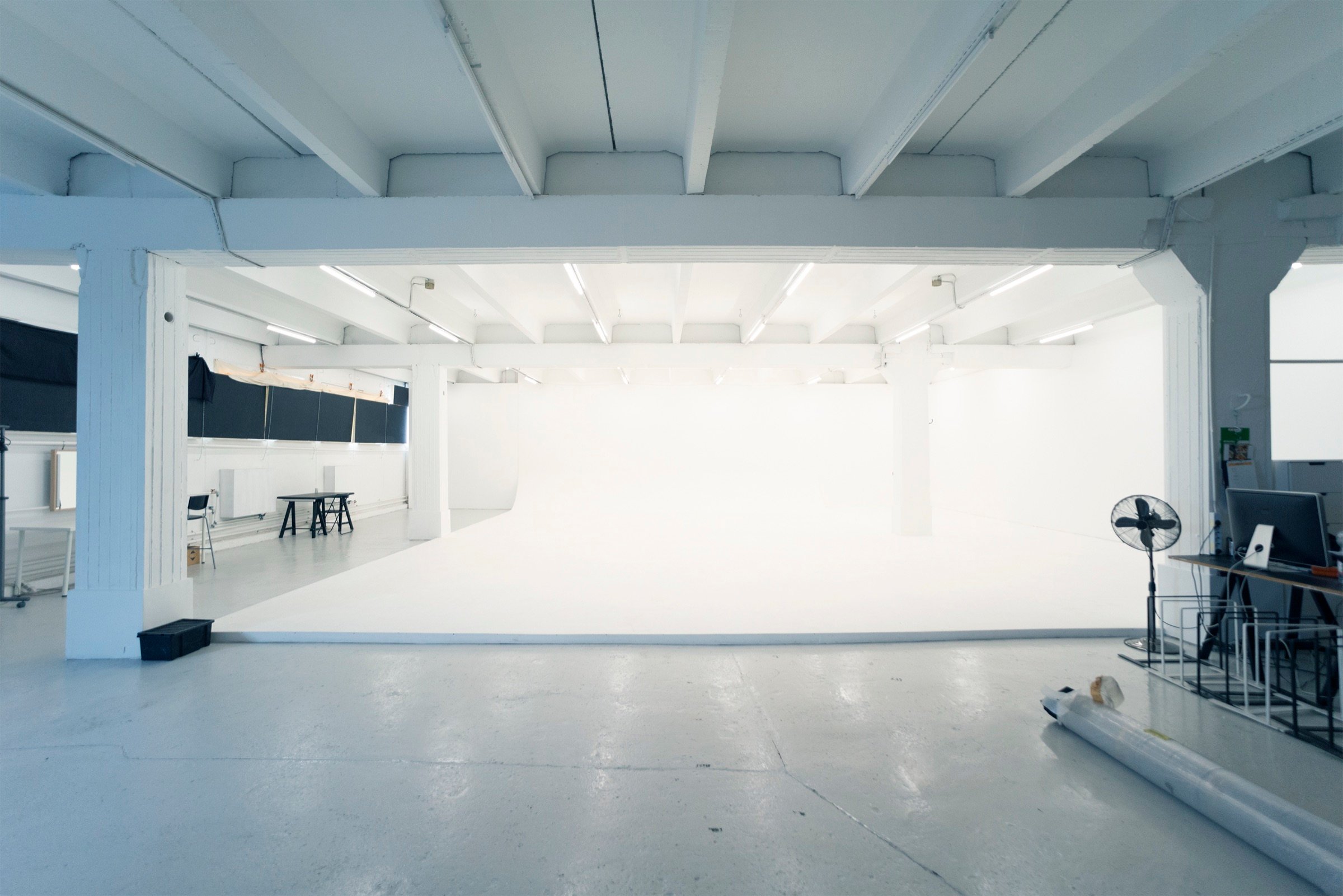 Picturepool Studios interior — wide view of the studio with a large white infinity cove, exposed ceiling beams, a workspace and black blackout curtains